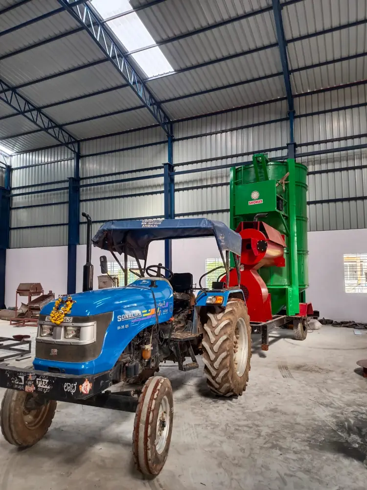 Shomas green tower type grain dryer with blower and a tractor in a workshop